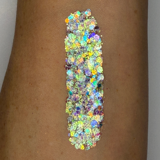 Close-up swatch of chunky cosmetic glitter applied to skin, featuring iridescent silver, aqua, blue, green, and holographic hexagonal glitter pieces in multiple sizes. The glitter is densely packed in a vertical swatch, creating a dazzling color-shifting sparkle effect with rainbow reflections and high-shine shimmer.