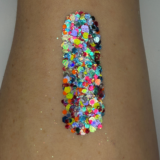 Close-up swatch of chunky cosmetic glitter applied to skin, featuring a vibrant mix of aqua blue, hot pink, lime green, purple, and iridescent hexagonal glitter pieces in multiple sizes. The glitter is densely packed in a vertical swatch, creating a colorful, carnival-inspired sparkle effect with holographic rainbow reflections and high-shine shimmer.