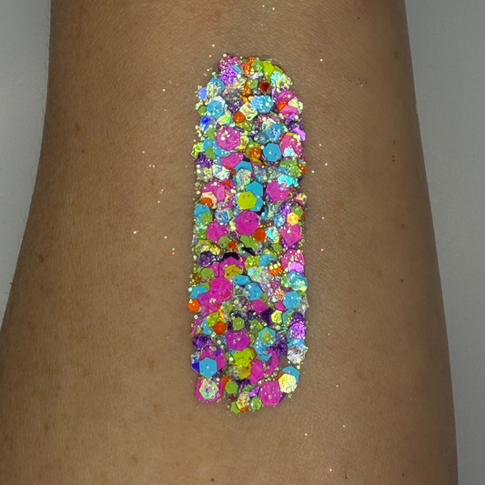 Close-up swatch of chunky cosmetic glitter applied to skin, featuring vibrant neon pink, aqua blue, lime green, and iridescent hexagonal glitter pieces in multiple sizes. The glitter is densely packed in a vertical swatch, creating a bold, electric sparkle effect with holographic rainbow reflections and high-shine shimmer.