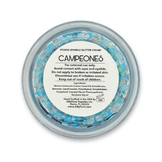 Bottom view of Campeones Studio Sparkle Glitter Cream by SillyFarm in a clear 25g jar, featuring sky blue and iridescent cosmetic glitter inspired by Argentina soccer fan colors, with product label visible on the base.
