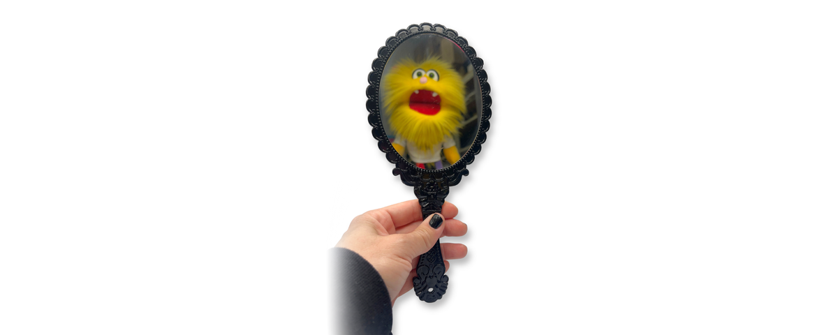 Ornate black handheld mirror for face painting and makeup with a playful reflection, perfect for revealing finished designs to clients.