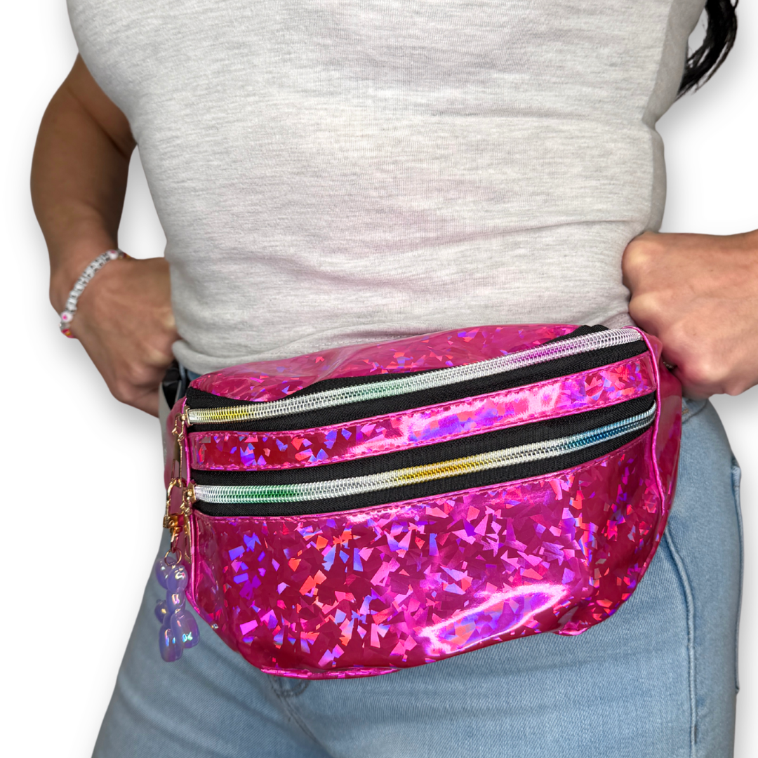 A person wearing a bright pink holographic waist bag with two rainbow zippers, shown from the chest down against a white background.