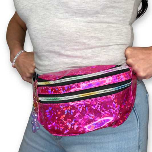 A person wearing a bright pink holographic waist bag with two rainbow zippers, shown from the chest down against a white background.