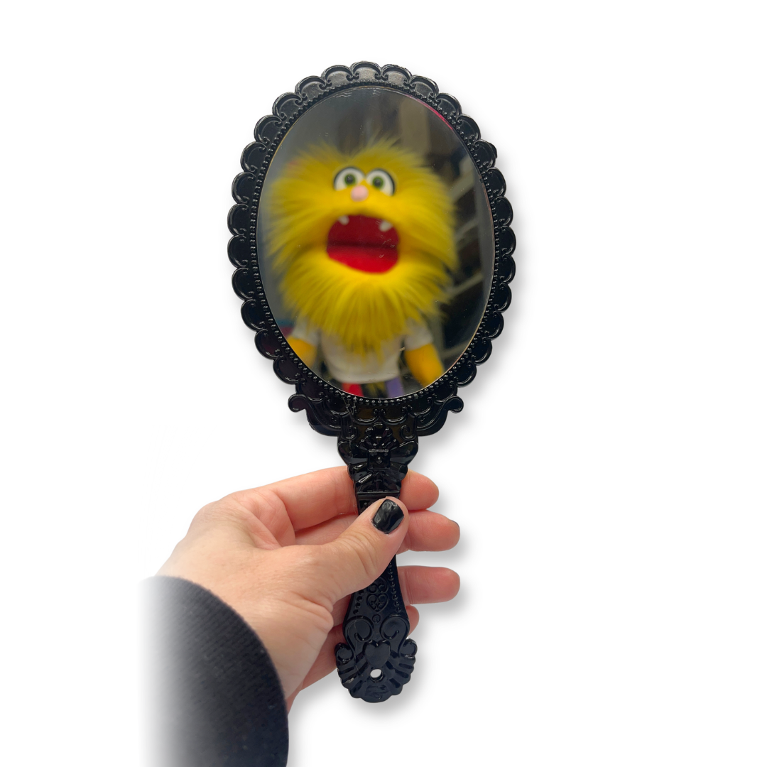 Hand holding a black decorative mirror with reflection of a yellow character on a white background