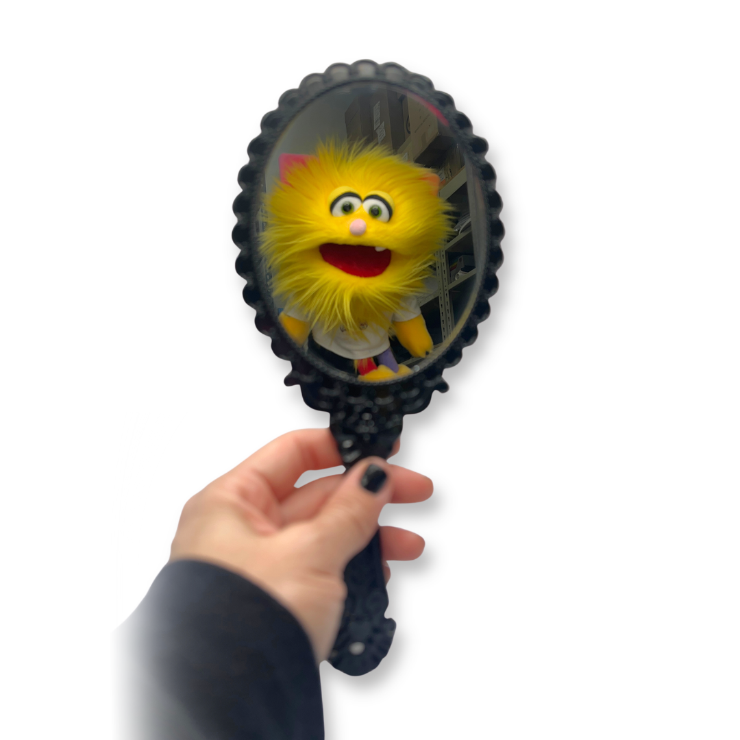 Hand holding a mirror with reflection of a yellow plush toy on a white background