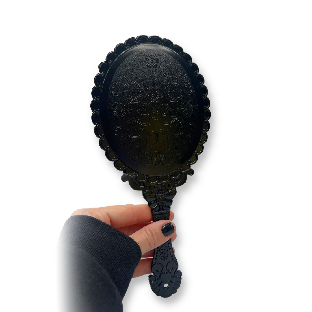 Back of a Black decorative hand mirror held by a hand on a white background