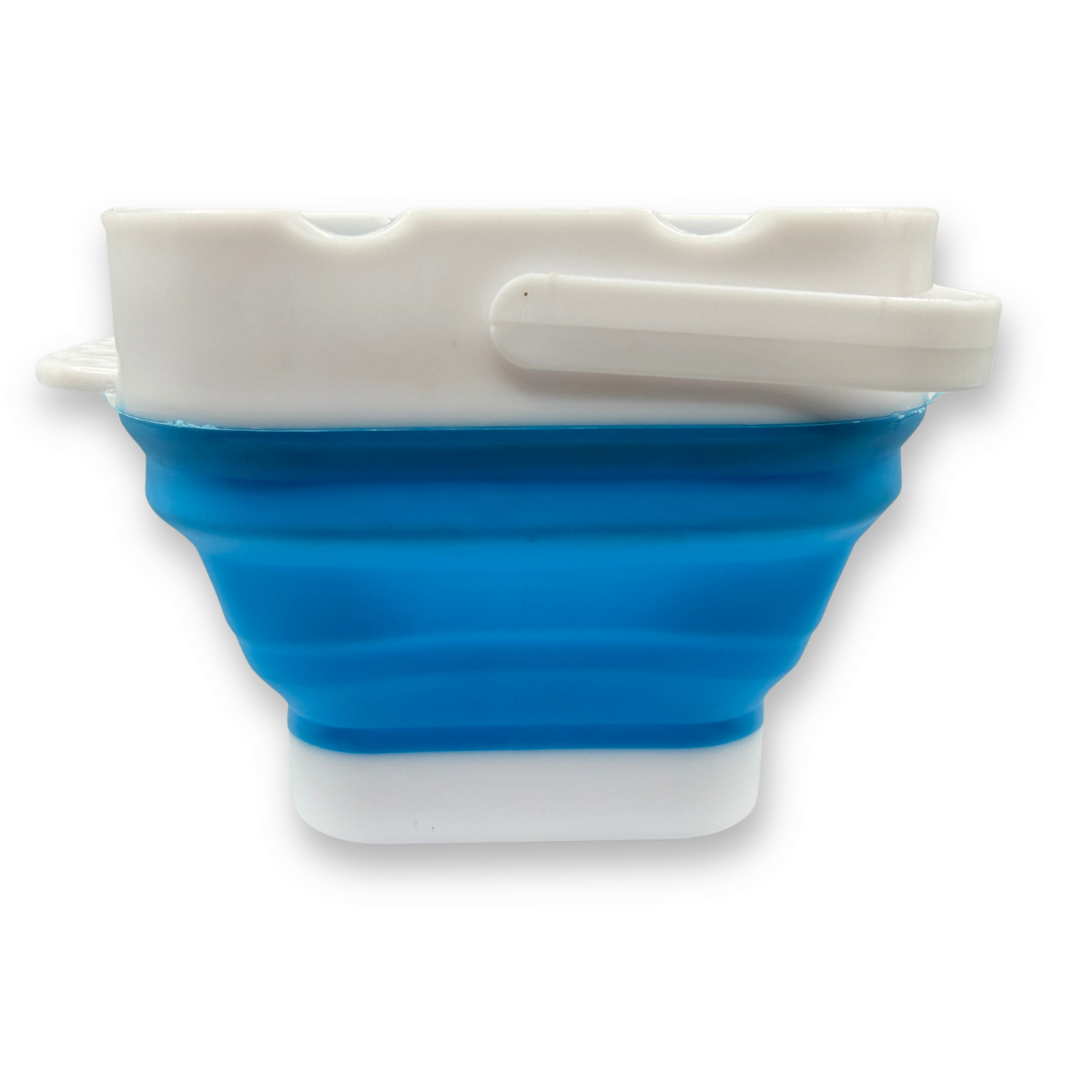 Side view of the blue SillyFarm Pop n Go Collapsible Water Cup showing the flexible silicone body, sturdy plastic rim, folding handle, and compact square shape.