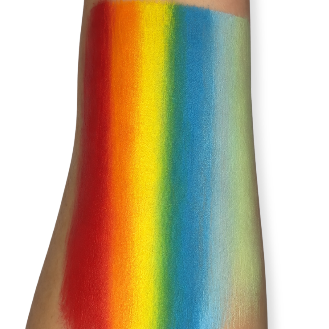 Close-up of a rainbow one stroke face paint swatch painted on a forearm, displaying blended bands of red, orange, yellow, green, blue, light blue, and white with smooth color transitions and high pigmentation.
