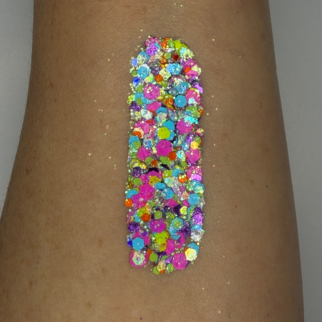 Close-up swatch of chunky cosmetic glitter applied to skin, featuring vibrant neon pink, aqua blue, lime green, and iridescent hexagonal glitter pieces in multiple sizes. The glitter is densely packed in a vertical swatch, creating a bold, electric sparkle effect with holographic rainbow reflections and high-shine shimmer.