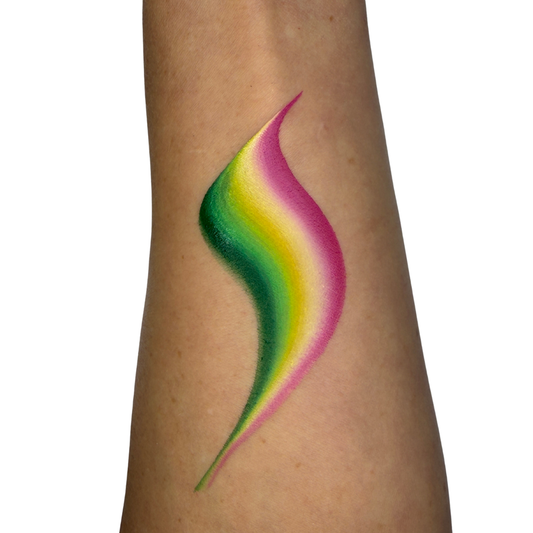 A swatch applied to a person's forearm, featuring a curved, S-shape with a smooth rainbow gradient of green, yellow, and pink on a plain white background.