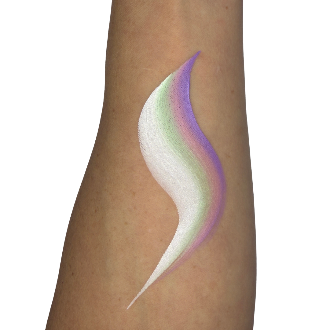 A close-up of a person's forearm with a decorative face paint swatch in a curved, layered shape. The swatch shows white at the front blending into pale green and lavender-purple at the back, against a plain white background.