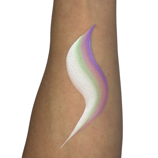 A close-up of a person's forearm with a decorative face paint swatch in a curved, layered shape. The swatch shows white at the front blending into pale green and lavender-purple at the back, against a plain white background.