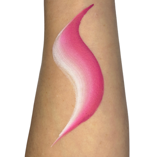 A close-up of a person's forearm with a large, smooth, S-shaped face paint swatch of pink and white gradient cream or powder makeup applied on the skin.