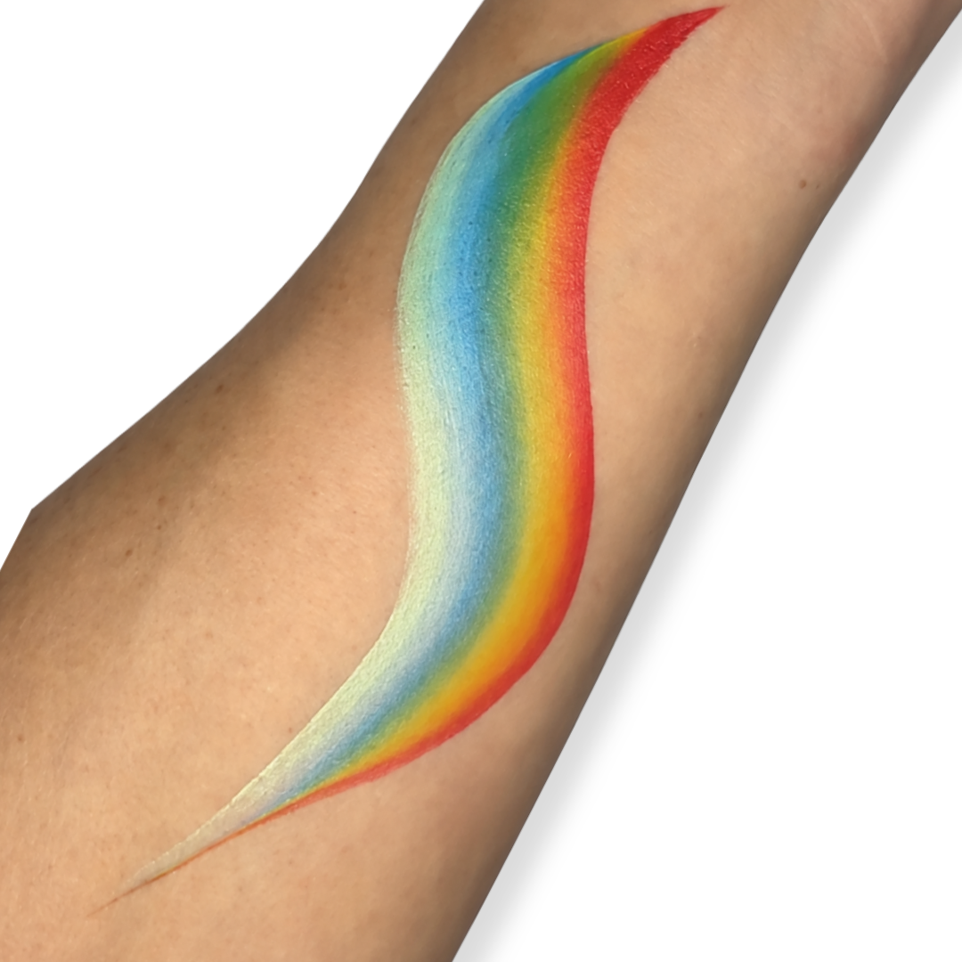 Close-up of a one stroke face paint rainbow brush stroke painted on a forearm, featuring smooth blended bands of white, light blue, blue, green, yellow, orange, and red in a flowing curved teardrop shape.