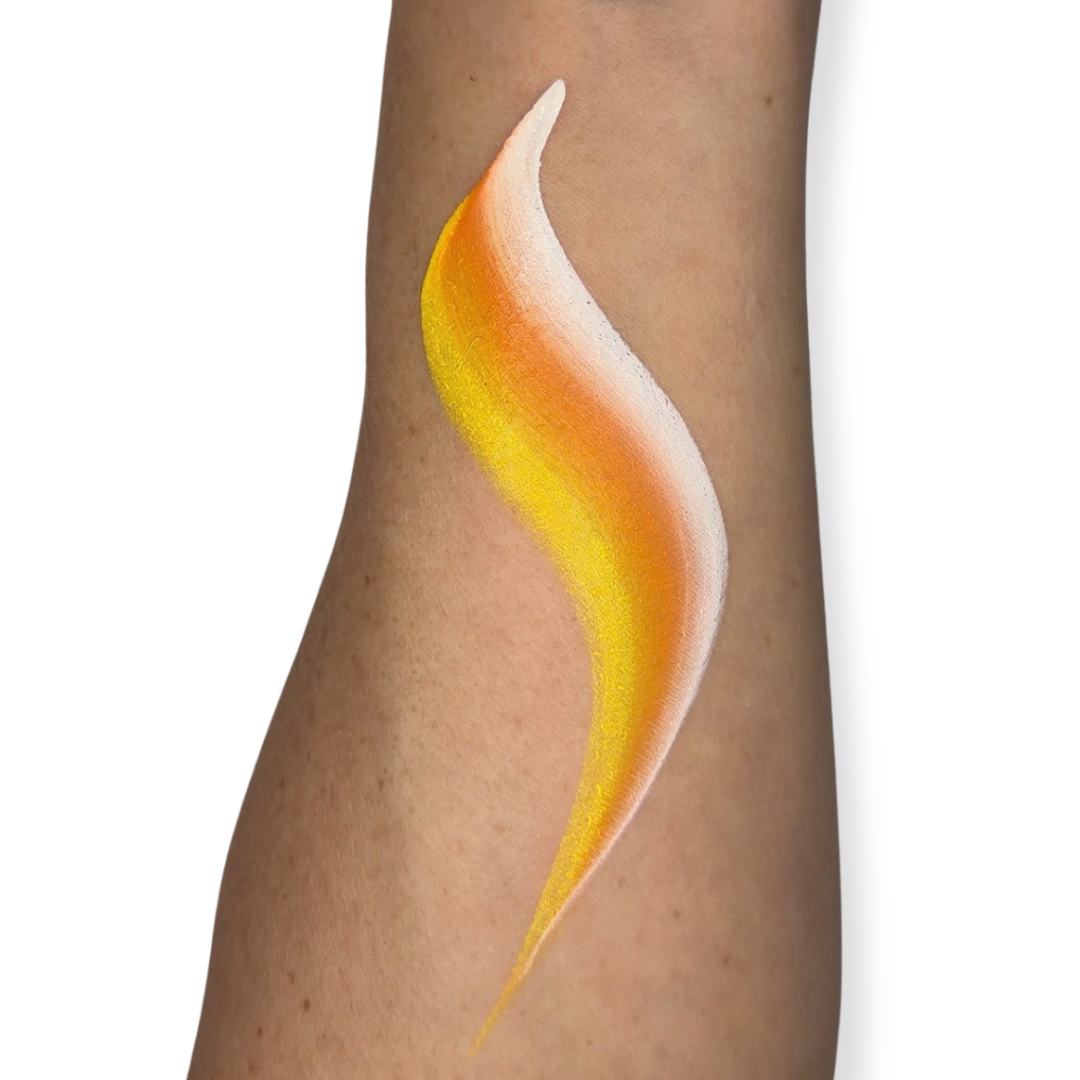 A close-up of a person's forearm with a face paint brush stroke in yellow, orange, and white on the skin, against a plain white background. The brush stroke looks like candy corn. 