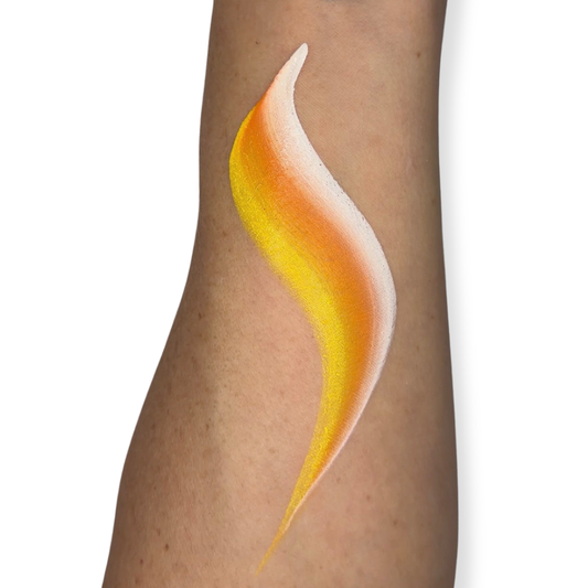 A close-up of a person's forearm with a face paint brush stroke in yellow, orange, and white on the skin, against a plain white background. The brush stroke looks like candy corn. 