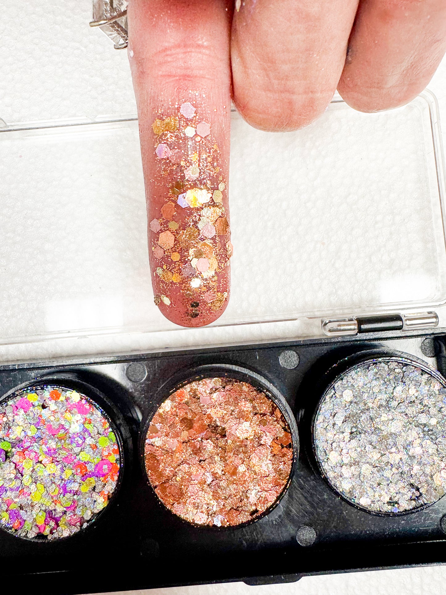 Close-up of a glittery nail polish with a compact of multicolored glittery powder.
