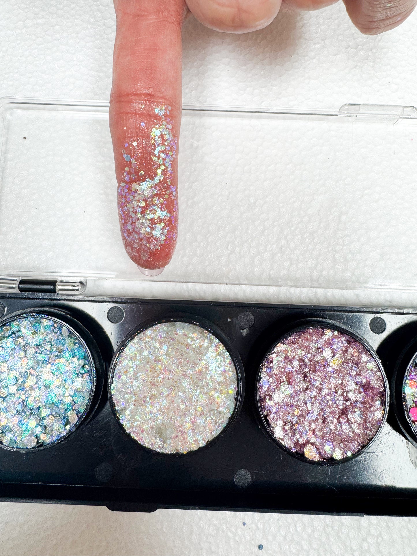 Glittery powder in a compact case with a finger applying glitter.