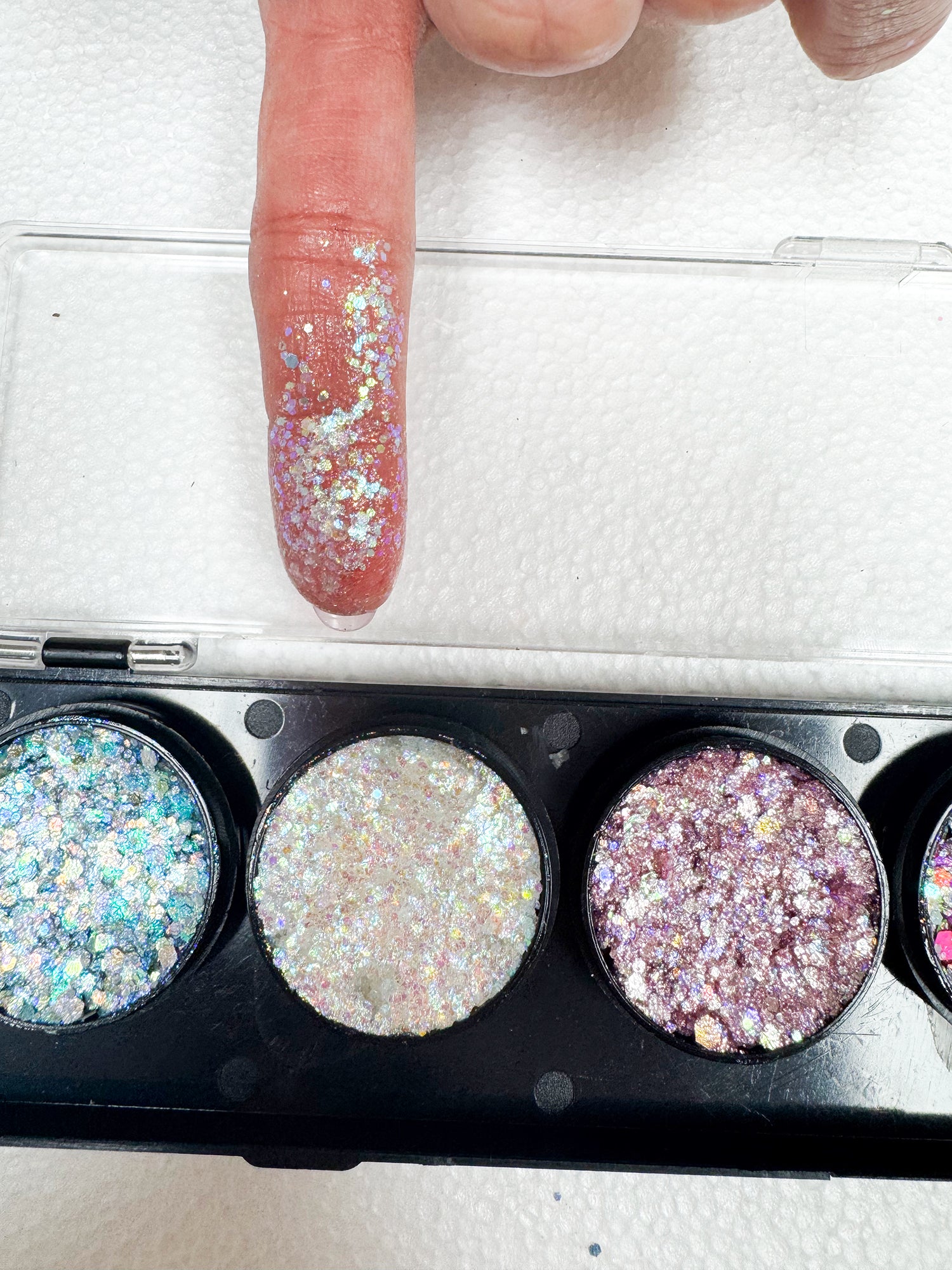 Glittery powder in a compact case with a finger applying glitter.