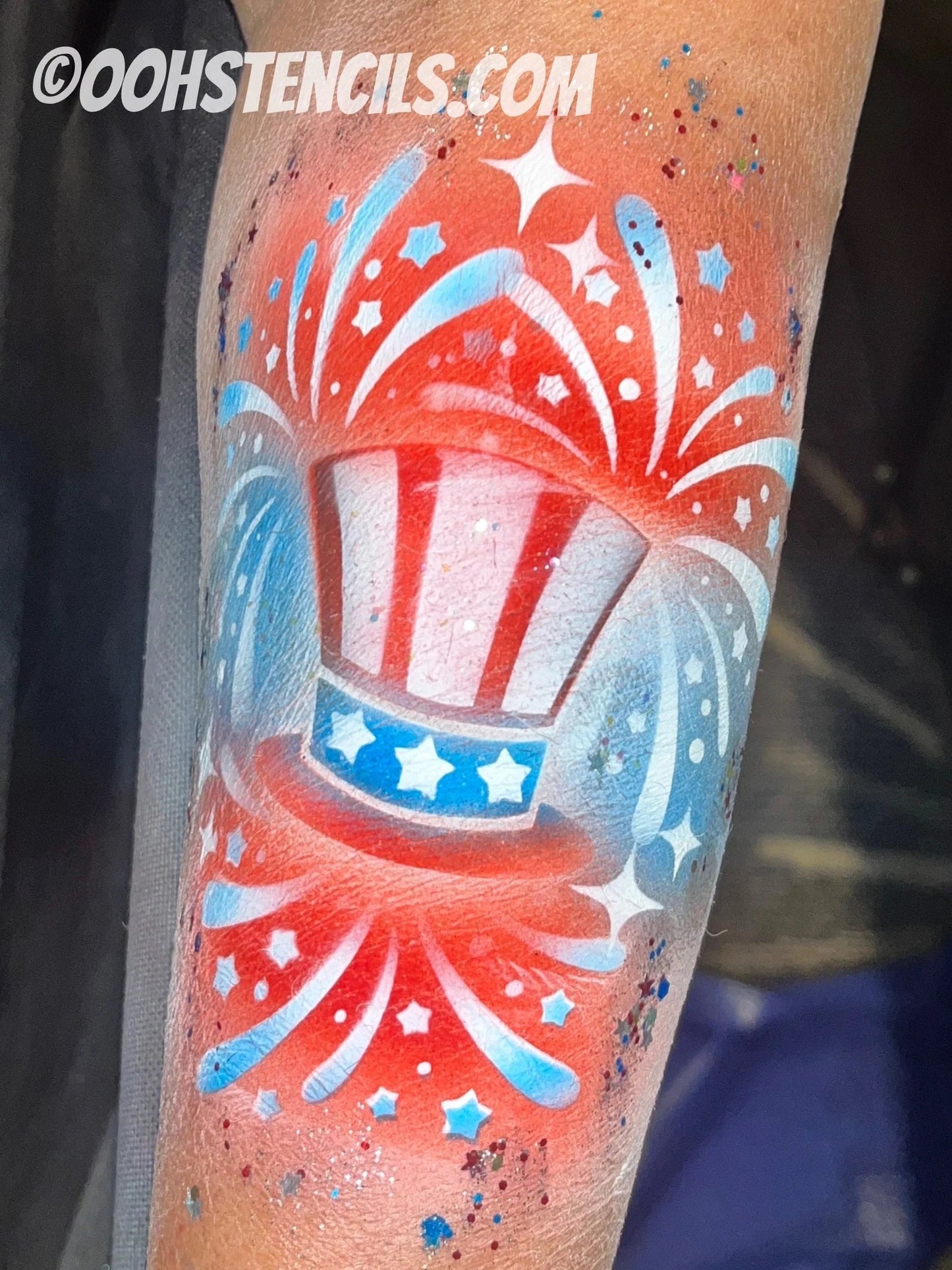 Patriotic Uncle Sam top hat face paint design on an arm featuring red, white, and blue fireworks, stars, sparkles, and glitter accents. Created using a stencil and blended face paint for a festive Fourth of July look.